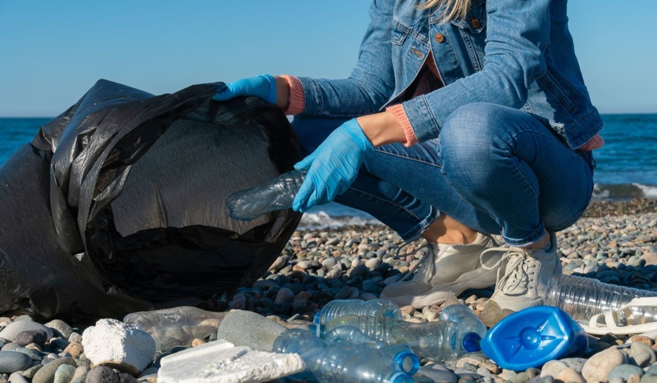 Image of woman picking up rubbish on beach.
